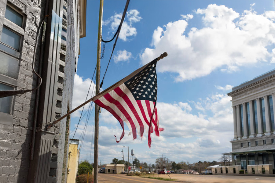 Old, faded, and torn American flag flying in breezy weather showing signs of wear